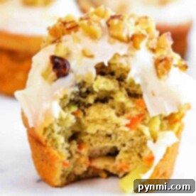 Wholesome Apple Carrot Muffins 6 A partially eaten apple carrot muffin with frosting and chopped nuts rests on a white surface.