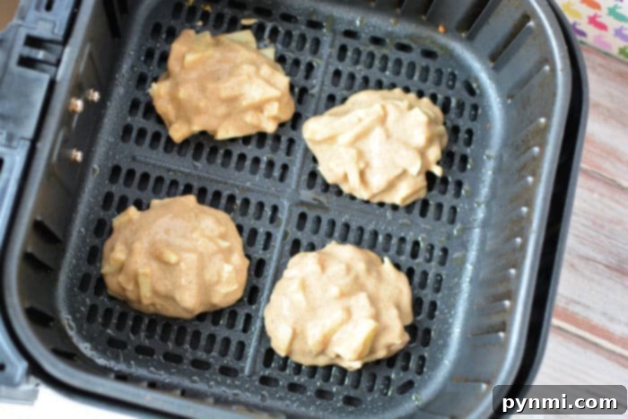 Four golden-brown air fryer apple fritters cooking in a mesh air fryer basket.