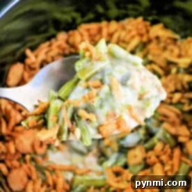 A spoon gently scoops the savory slow cooker green bean casserole, capturing its rich aroma and creamy texture.