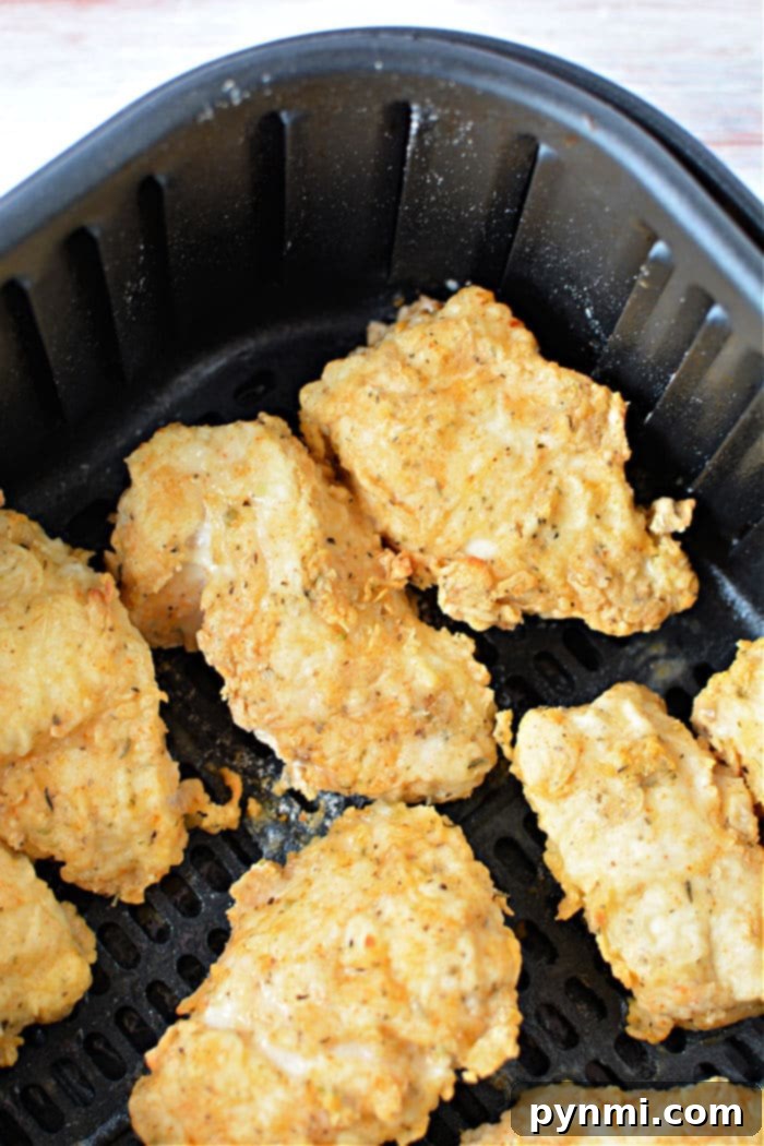 Stacked plates of golden-brown air fryer fried chicken breasts, garnished with fresh herbs.