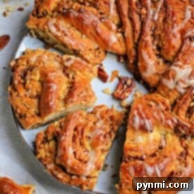 A spiral pecan cinnamon roll with icing, meticulously crafted like a bread wreath, features enticing slices on a white plate beside a bowl of pecans.