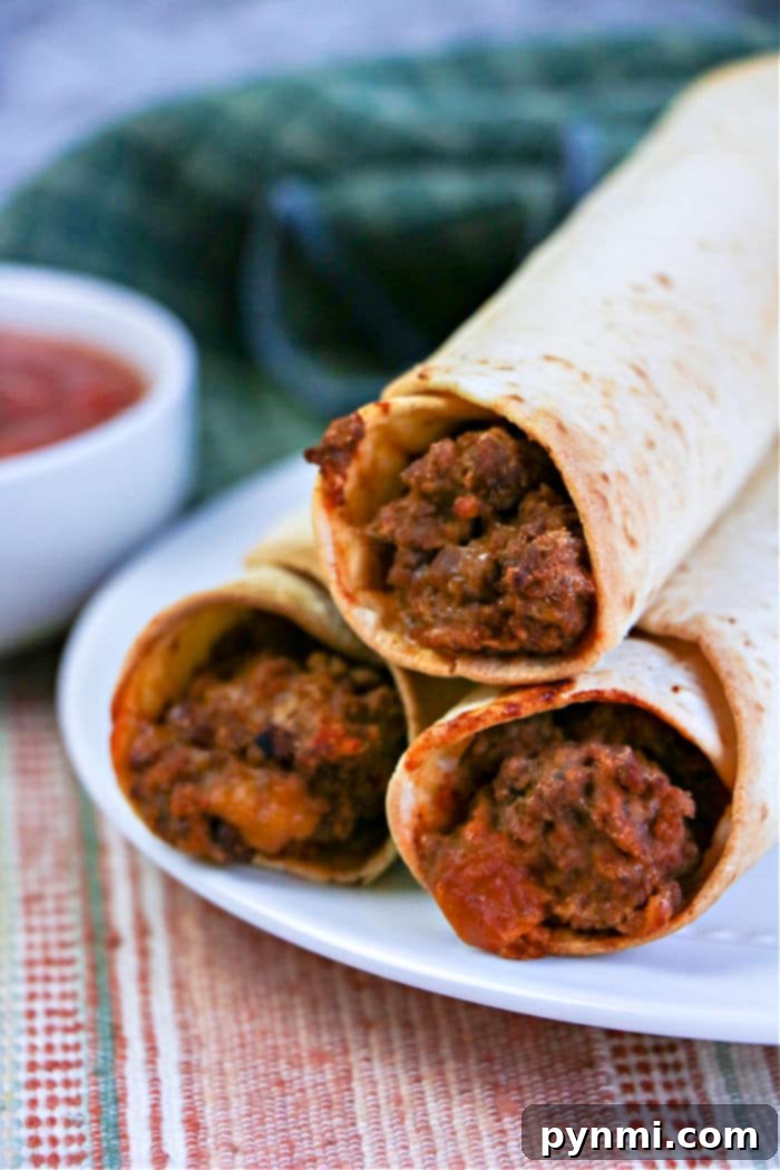 Crispy Air-Fried Flautas 2 Three crispy air fryer flautas, rest invitingly on a white plate while a bowl of zesty salsa tempts in the background, ready to be enjoyed.