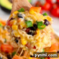 Instant Pot Mexican Fiesta Chicken and Rice 10 A wooden spoon holding cheesy rice with black beans, corn, bell peppers, and green onions from a savory Instant Pot Mexican chicken and rice dish.