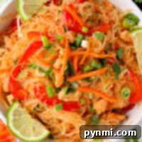 A bowl of rice noodles with chicken, carrots, bell peppers, and green onions, perfectly capturing the flavors of instant pot Pad Thai, garnished with fresh lime wedges.