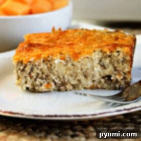 A slice of savory breakfast cheese grits casserole sits on a white plate with a fork beside it.
