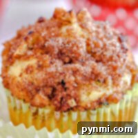 Close-up of an apple zucchini muffin topped with crumbly cinnamon sugar and nuts, nestled in a yellow paper liner.