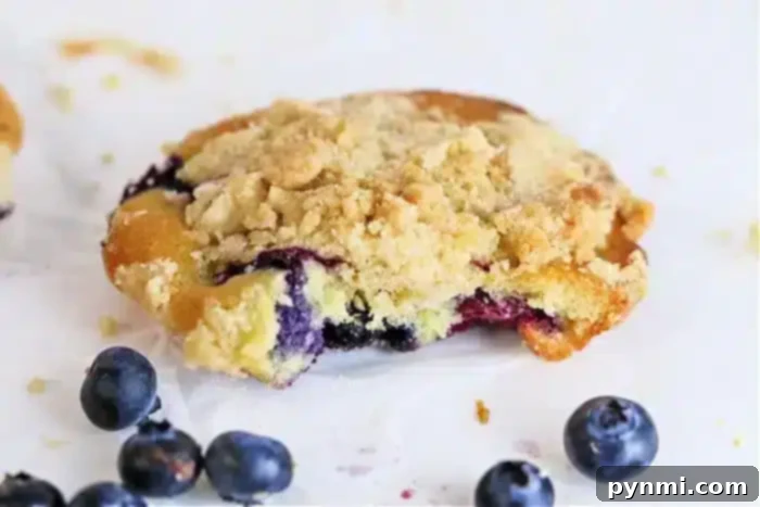 Blueberry Muffin Top Mastery 7 A crumbly pastry reminiscent of blueberry muffin tops, with a rich blueberry filling and topped with streusel, sits on a white surface. Several whole blueberries are scattered around.