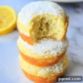 Fluffy Bisquick Muffins in Minutes 10 Three lemon Bisquick muffins stacked, powdered sugar dusted on top, with a bite taken from the top muffin. A fresh lemon slice lingers in the background.
