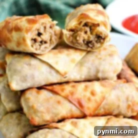 A plate stacked with several golden-brown ground beef egg rolls. The top egg roll is halved, revealing a delicious filling of savory meat and vegetables. A green cloth is partially visible in the background.