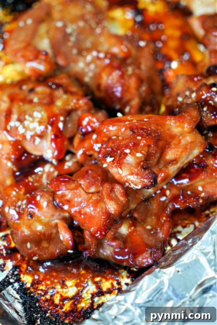 Close-up of teriyaki glazed, baked teriyaki chicken thighs sprinkled with sesame seeds on a foil-lined tray.