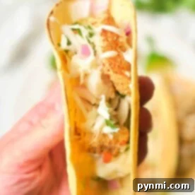 A hand holding a taco filled with crispy air fryer fish, coleslaw, and garnished with fresh herbs, ready to be enjoyed.