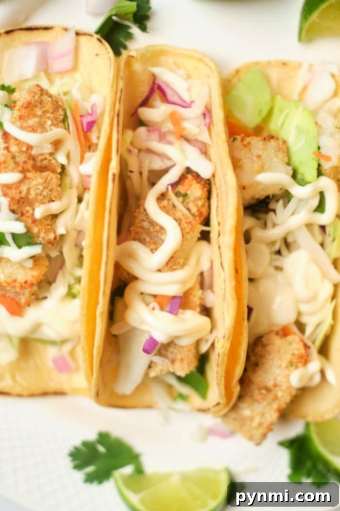 Crispy Air Fryer Fish Tacos 8 Two fully assembled fish tacos in soft tortillas, garnished with a creamy white sauce and fresh cilantro, on a wooden board.