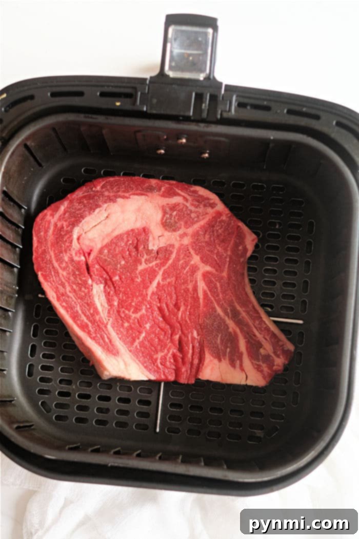 Close-up of a seasoned ribeye steak, ready to be cooked in an air fryer, showcasing its marbling and even spice coating.