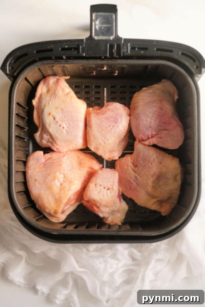 Mastering Frozen Chicken Thighs in Your Air Fryer 5 Four air fryer frozen chicken thighs with grill marks are shown being arranged in a hot air fryer basket.