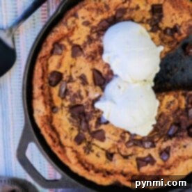 A cast iron chocolate chip cookie topped with two scoops of vanilla ice cream sits invitingly, a serving spatula by its side.