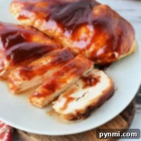Air fryer BBQ chicken breast, sliced and coated in tangy barbecue sauce, served on a white plate atop a wooden board.