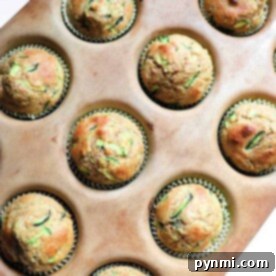 A muffin tray holds 12 freshly baked zucchini applesauce muffins, each nestled perfectly in paper liners.