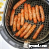 Sausage links in an air fryer basket rest on a sleek black perforated tray.