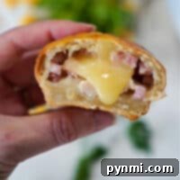 A hand holds a baked bread roll reminiscent of air fryer chicken cordon bleu, filled with melted cheese and small pieces of ham. A bite reveals the gooey interior, while greenery and other ingredients blur in the background.