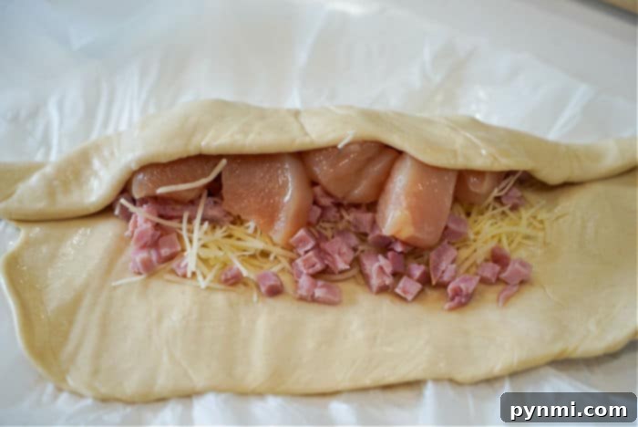 Unbaked pastry filled with diced chicken, grated cheese, and chicken pieces awaits transformation into a delicious air fryer chicken cordon bleu on parchment paper.