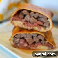 Close-up of a sandwich with layers of beef and cheese, reminiscent of a deconstructed beef Wellington, cut in half and stacked on a plate.
