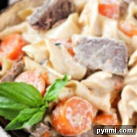 Savor the creamy pasta with tender beef chunks, reminiscent of a crockpot beef stroganoff, topped with carrot slices and a basil garnish in a bowl.