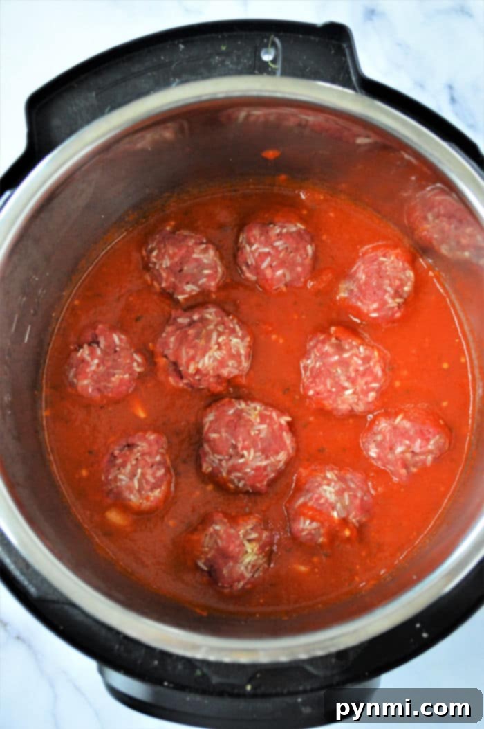 Effortless Instant Pot Porcupine Meatballs 4 An instant pot filled with raw porcupine meatballs nestled in a rich red tomato sauce, ready for cooking. The cooker sits elegantly on a marble countertop.