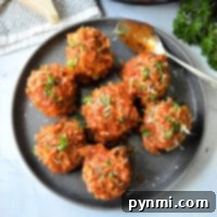 A plate with seven instant pot porcupine meatballs covered in tomato sauce and garnished with chopped herbs. A spoon rests on the plate, while a piece of cheese and parsley linger in the background.