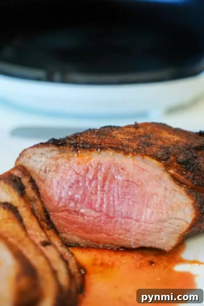 Ultimate Air Fryer Tri Tip 9 Close-up of sliced, air fryer-grilled tri tip with a medium-rare center. The steak is juicy, with a charred outer layer, resting on a white surface. A small amount of juice is pooled around the slices, highlighting the meat's tenderness.