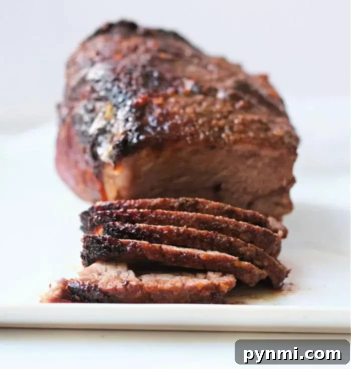 A roasted air fryer roast beef meatloaf placed on a white surface, the meatloaf is browned on the outside. In the foreground, several slices of the meatloaf are cut and displayed.