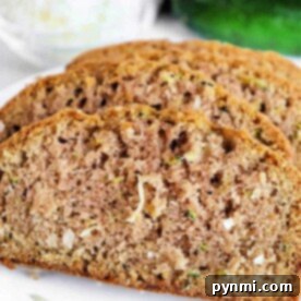 Slices of coconut zucchini bread are artfully arranged on a white plate, with a fresh whole zucchini in the background.