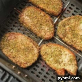 Seasoned pork chops, or pork steak in air fryer, cook to golden brown perfection, evenly spaced in the basket.