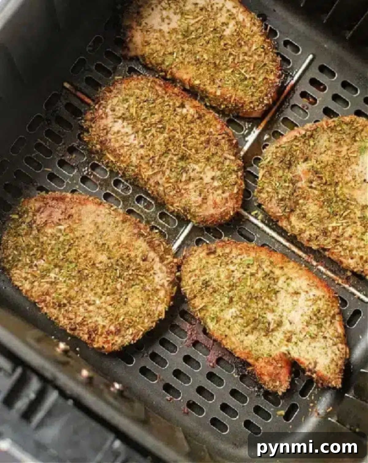 Perfect Air Fryer Pork Steak 7 Seasoned pork chops, or pork steak in air fryer, cook to golden brown perfection, evenly spaced in the basket.