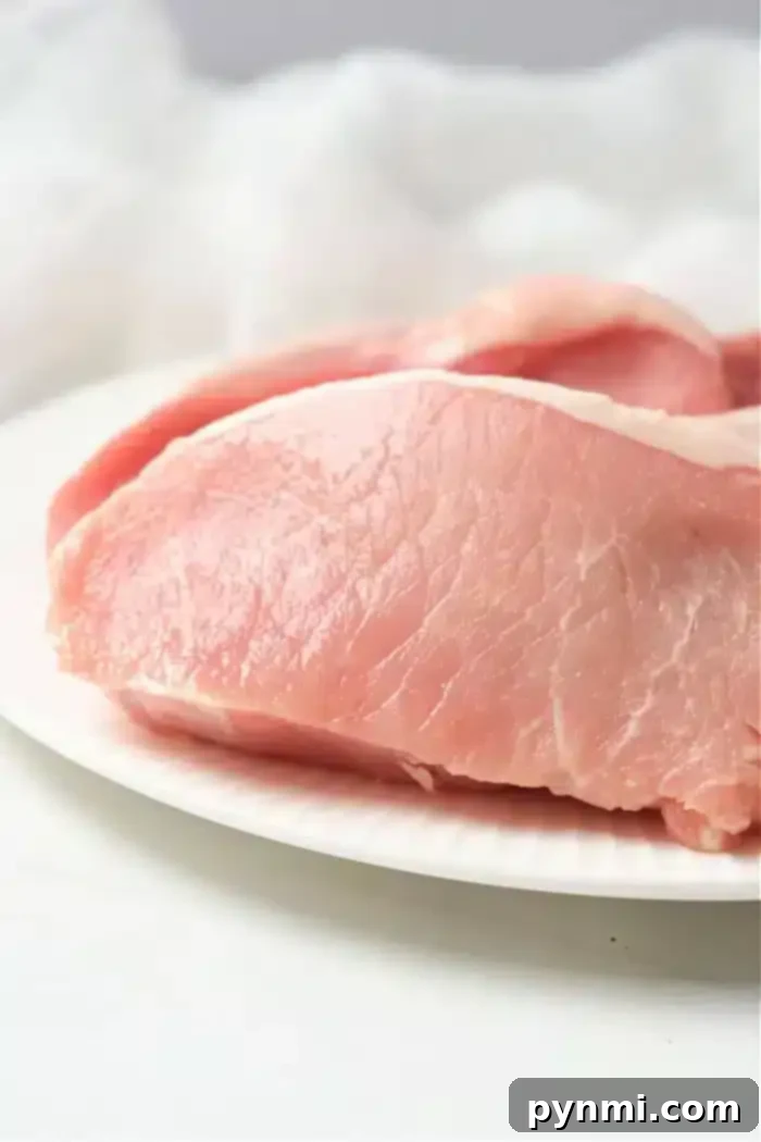 Perfect Air Fryer Pork Steak 9 Close-up of raw, boneless pork chops prepared for an air fryer on a white plate. The fresh, pink meat boasts visible marbling against a softly blurred, white background.