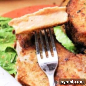 Close-up of a fork holding a slice of breaded pork chop, perfectly crisped in the air fryer, with leafy greens on a plate.
