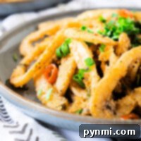 Fried calamari, a testament to mastering how to cook calamari perfectly, is garnished with chopped herbs on a gray plate, set on a patterned cloth.