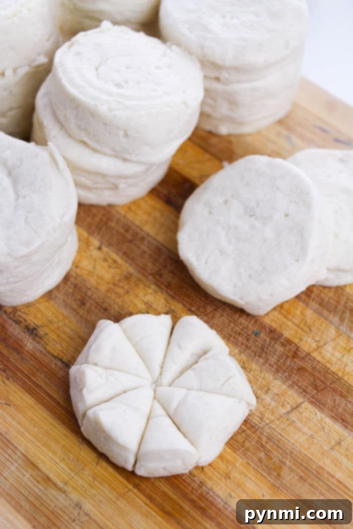 Pull-Apart Monkey Bread Muffins 4 Stacks of uncooked biscuit dough, perfect for making Monkey Bread, rest on a wooden board, with one sliced into eight pieces.