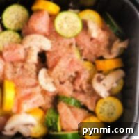 Air fryer chicken and vegetables come together with raw chicken, mushrooms, and sliced squash perfectly seasoned in an air fryer basket.