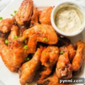 A plate of hot wings cooked to perfection in the air fryer is garnished with green onions and served alongside a small bowl of creamy dipping sauce.