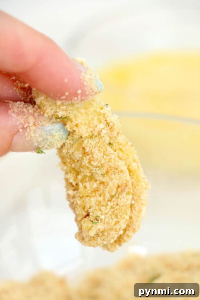 A hand holds a breaded artichoke heart piece above a bowl of breadcrumbs, reminiscent of preparing air fryer artichoke hearts.