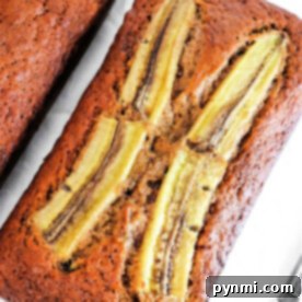 A loaf of ginger banana bread with sliced bananas on top rests elegantly on a pristine white surface.