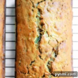 A golden brown loaf of gingerbread-zucchini bread rests on a cooling rack, its inviting aroma filling the air, with a charming crack adorning its top.