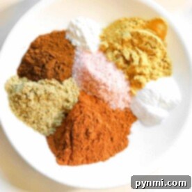 A white plate with piles of vibrant spice powders, including gingerbread spice ingredients, and coarse salt, arranged artfully.