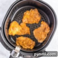 Four perfectly seasoned chicken thighs nestled in an air fryer basket, ready to transform into crispy fried delights.