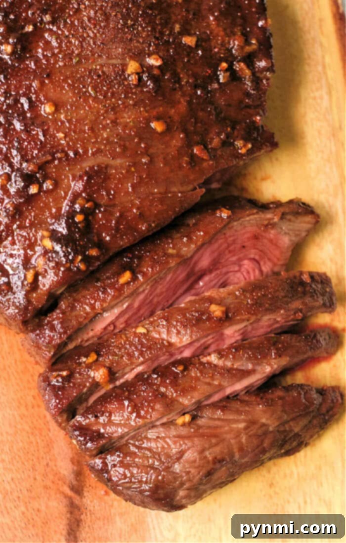 Flavor-Packed Air Fryer Dry Rub Flank Steak 2 Sliced, juicy flank steak with a seared crust and garlic seasoning sits elegantly on a wooden cutting board, reminiscent of perfectly cooked air fryer flank steak.