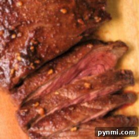 Sliced, juicy flank steak with a seared crust and garlic seasoning sits elegantly on a wooden cutting board, reminiscent of perfectly cooked air fryer flank steak.