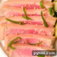 Slices of seared ahi tuna steak with sesame seeds and green garnishes on a white plate, prepared perfectly in an air fryer.