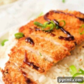 A plate with white rice topped with sliced, air fryer chicken katsu drizzled with dark sauce and garnished with sliced green onions.