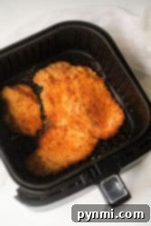 Breaded chicken cutlets, reminiscent of air fryer chicken katsu, are cooking in an air fryer basket.