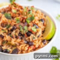 A bowl of rice mixed with instant pot black beans, diced vegetables, and garnished with cilantro and lime wedges, showcasing a healthy and vibrant meal.
